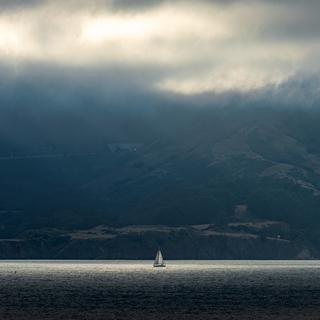 A sailboat in a gap between the clouds, as seen from across the Golden Gate.